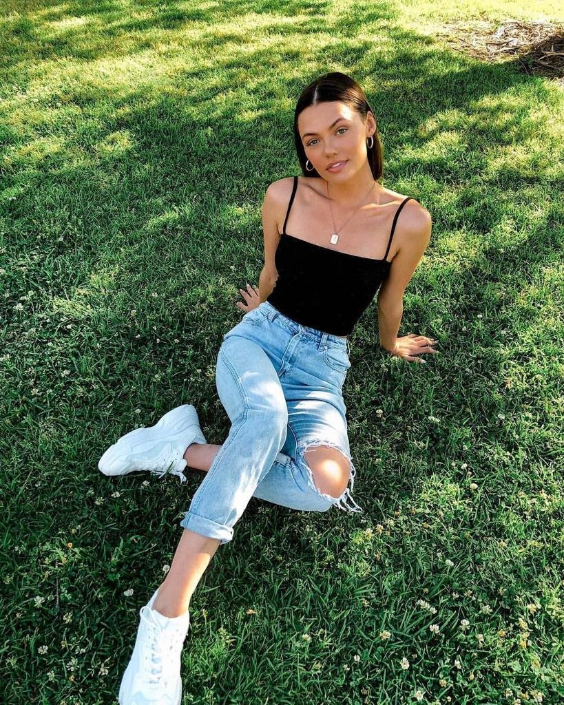 Top negro con jeans rotos sentada en el césped