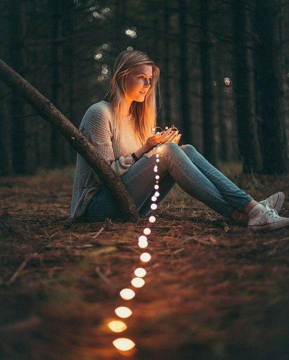 Chica sentada en el bosque con una hilera de luces
