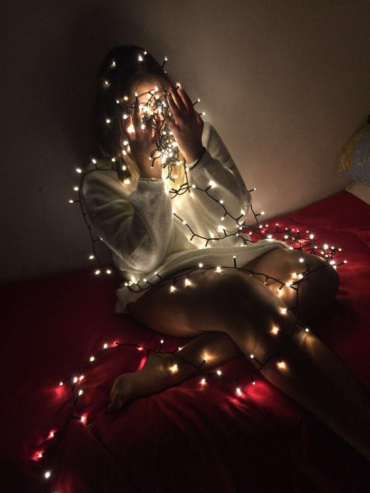 Chica sentada en la cama con luces entre las manos