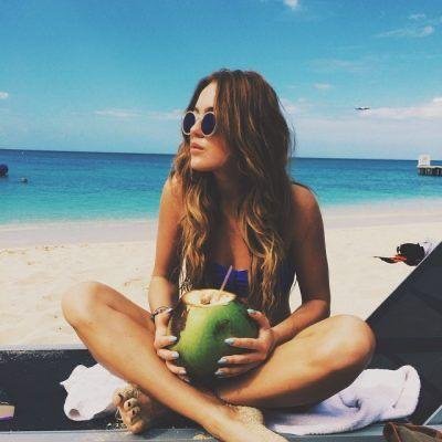 Chica sentada en la arena con un coco entre las manos