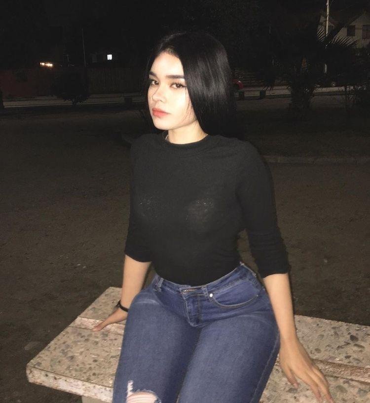 Chica de pie de noche con top negro y jeans
