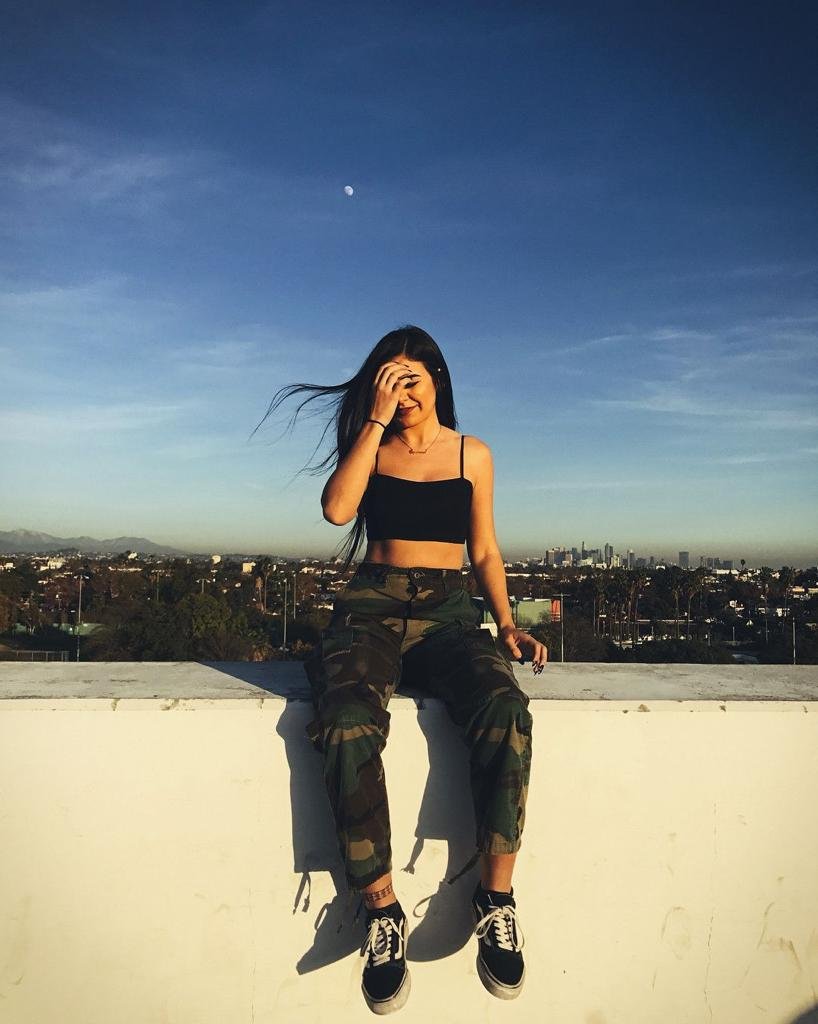 Chica sentada en un muro con la ciudad de fondo