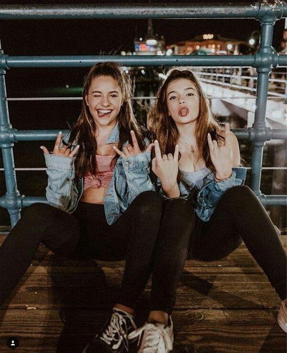 Dos amigas sentadas en el suelo de un muelle con chaquetas vaqueras