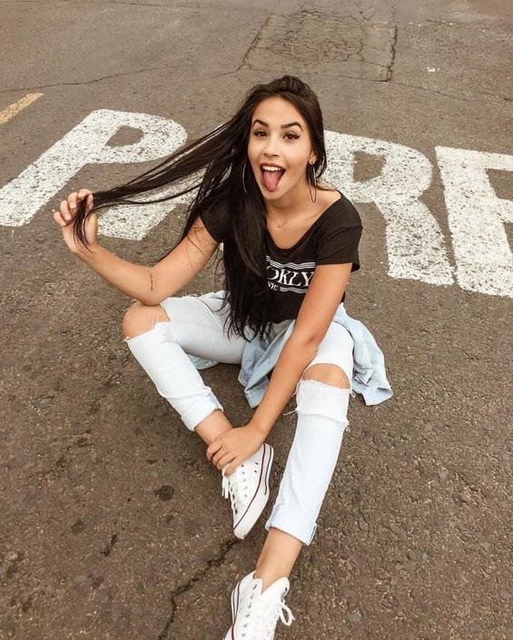 Chica sentada en el asfalto con jeans rotos
