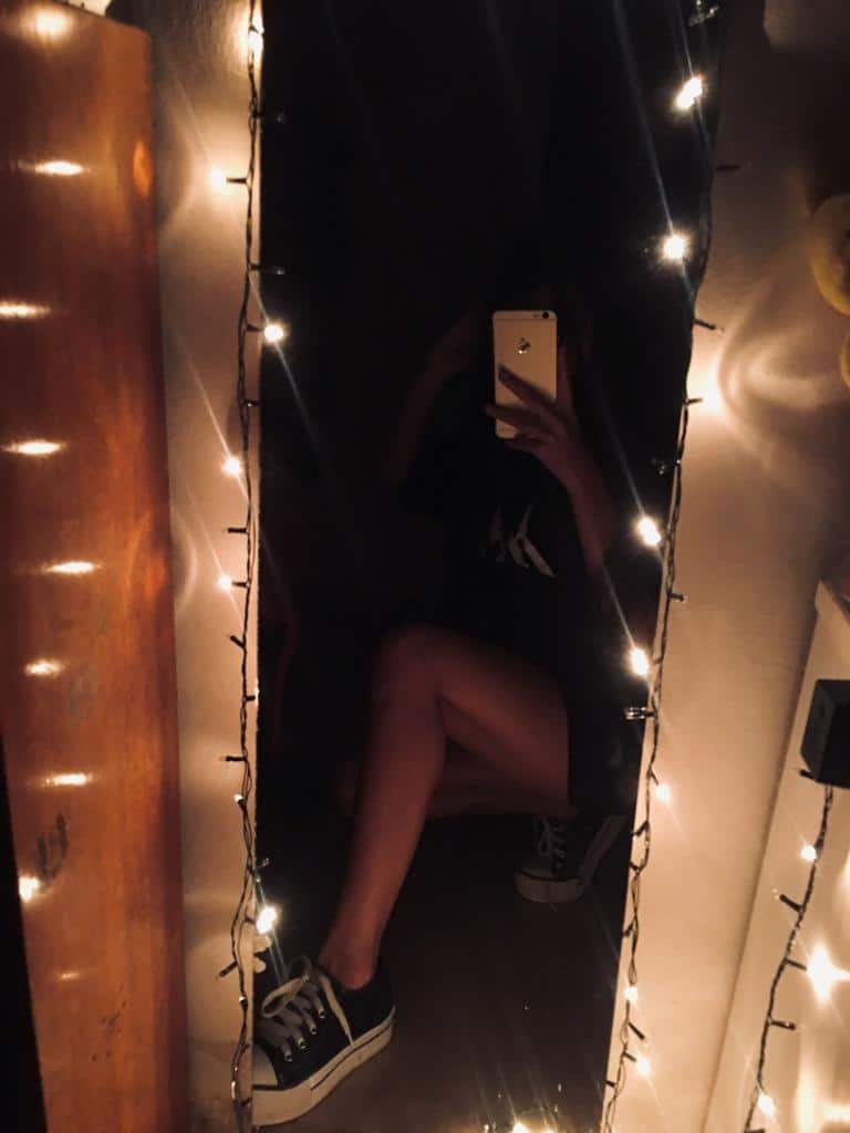 Espejo rodeado de luces con una chica sentada delante