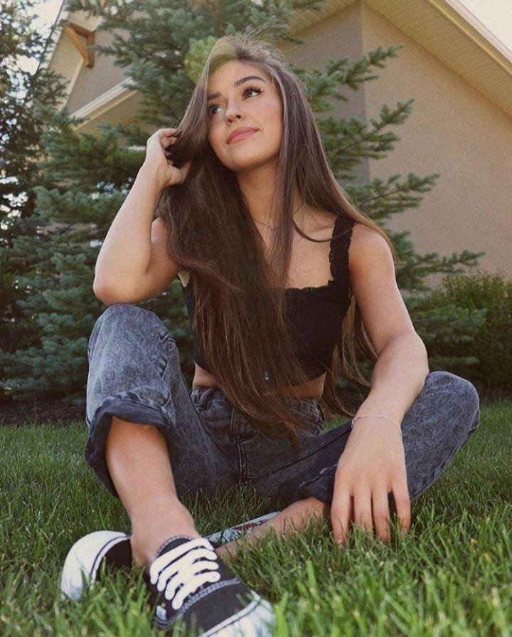 Chica sentada en el césped con jeans y tenis