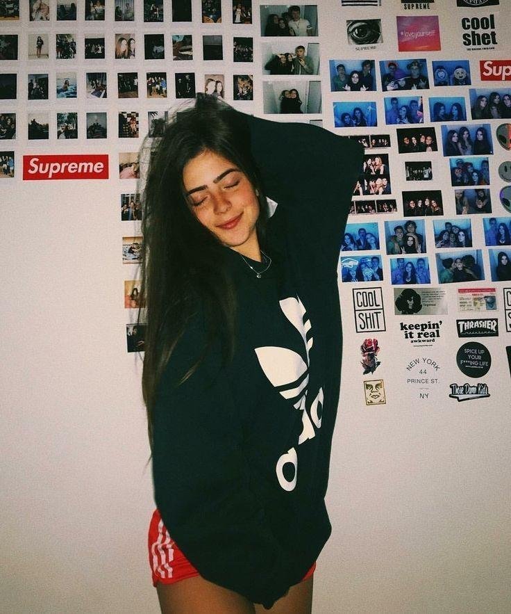 Chica con sudadera oversize apoyada en una pared de fotos