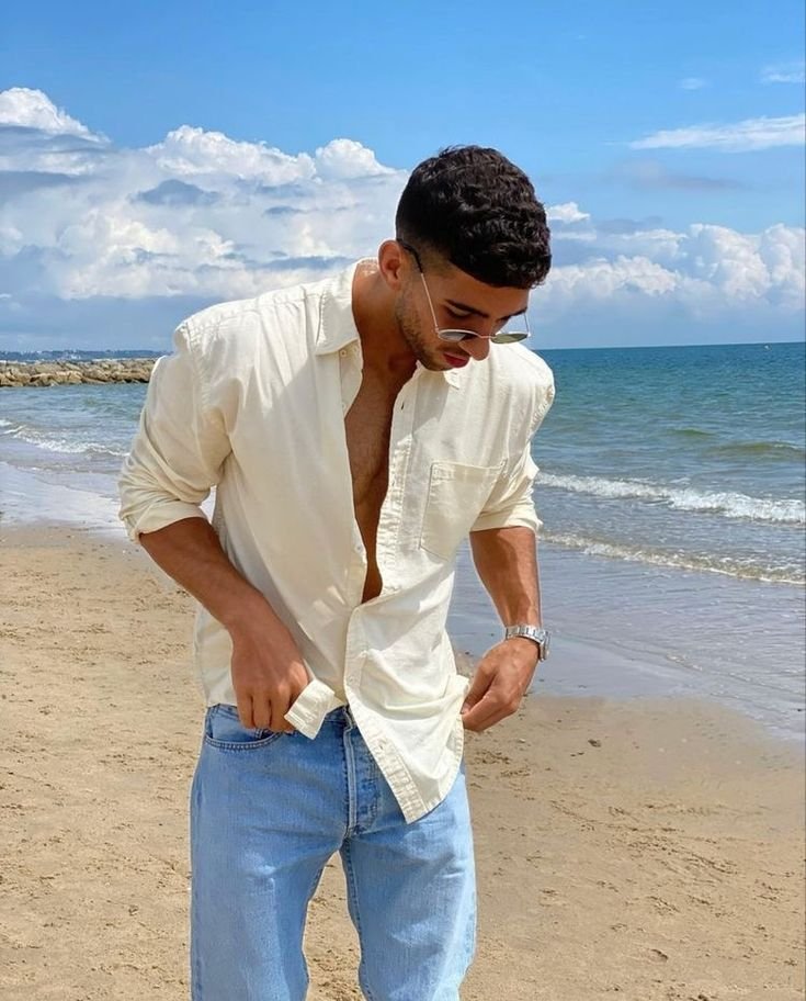 Chico en la playa con camisa blanca y jeans