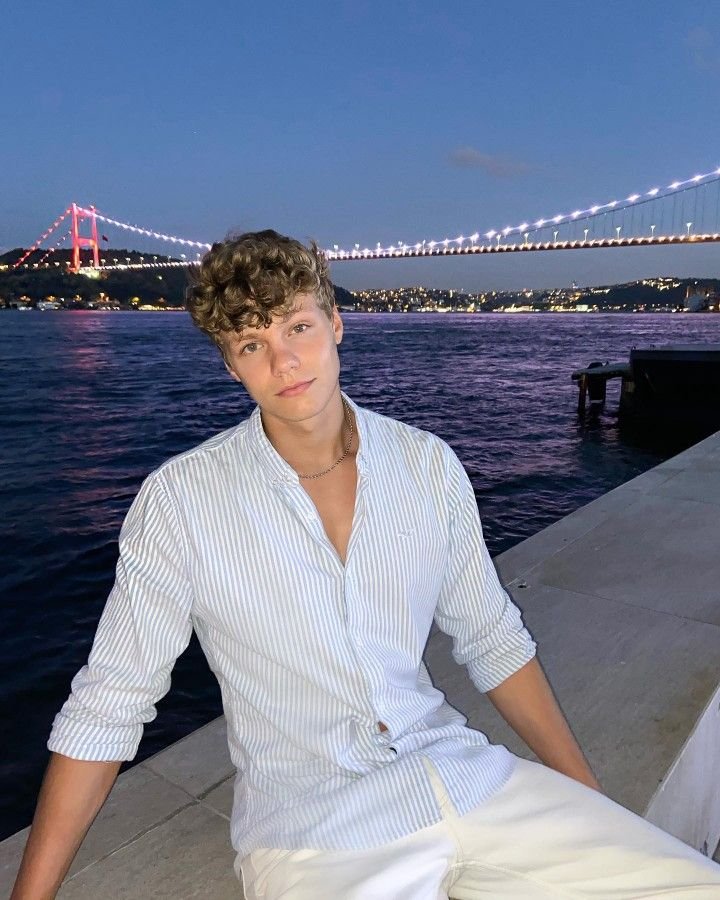 Chico sentado junto al mar con camisa blanca