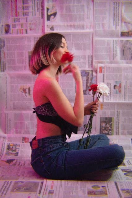 Chica sentada en el suelo oliendo una rosa con fondo rosa