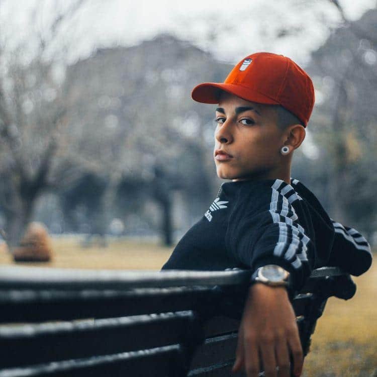 Chico de perfil sentado en un banco con gorra mirando a lo lejos