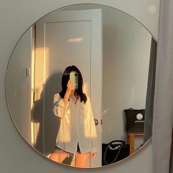 Cuerpo entero reflejado en un espejo redondo con luz de sol