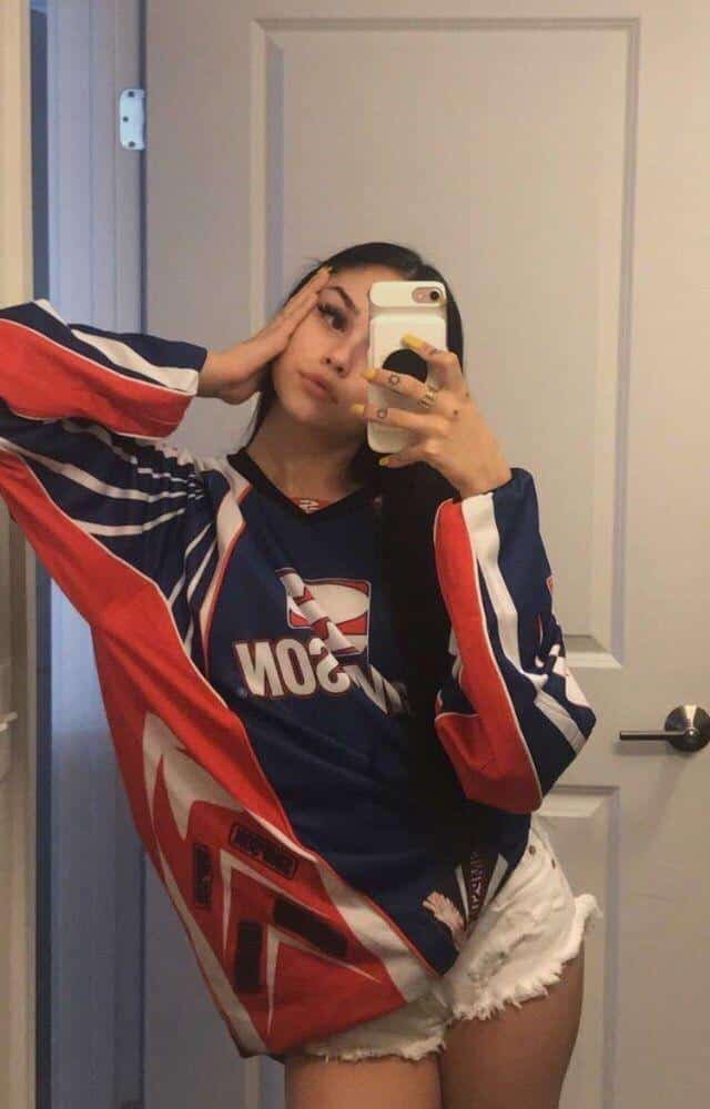 Pose de pie con sudadera roja y la mano cerca de la cara
