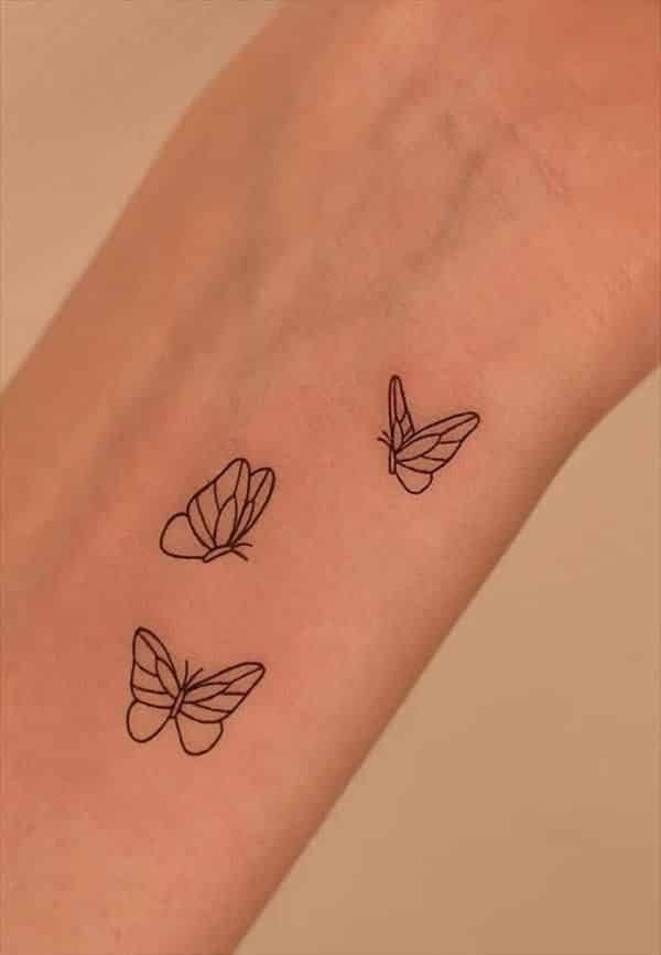 Tres mariposas de línea fina tatuadas en el antebrazo
