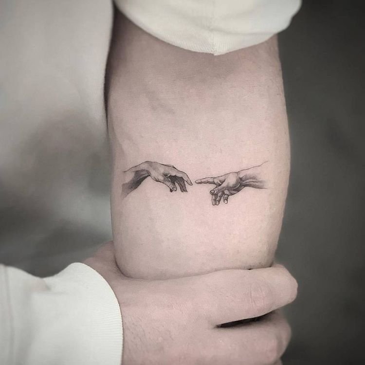 Las manos de la Creación tatuadas en línea fina en el brazo