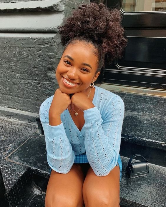 Dos chongos afro con suéter azul, sentada en unas escaleras