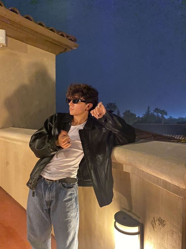Chico apoyado en un muro al atardecer con chaqueta de cuero