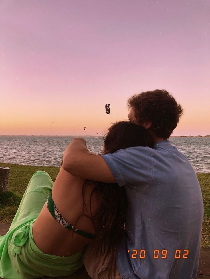 Pareja abrazada sentada en la playa al atardecer