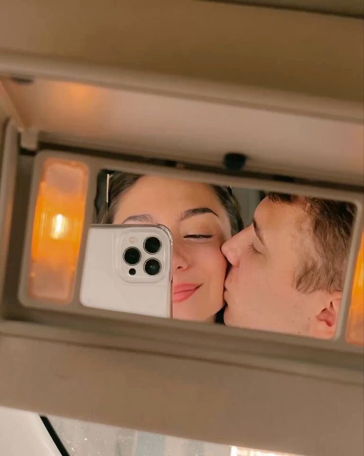 Selfie de pareja en el retrovisor del coche dándose un beso