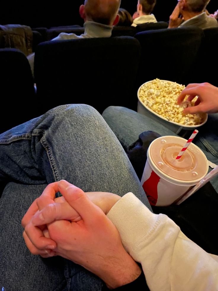Manos entrelazadas en el cine con palomitas