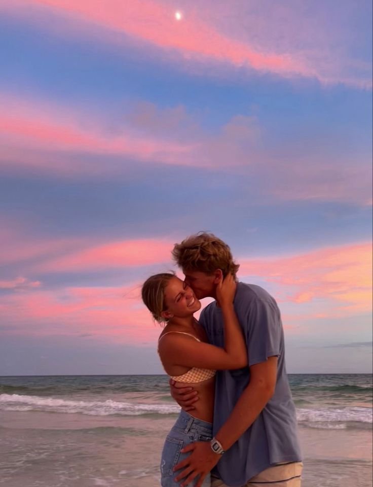 Pareja abrazada en la playa con el cielo rosa al atardecer