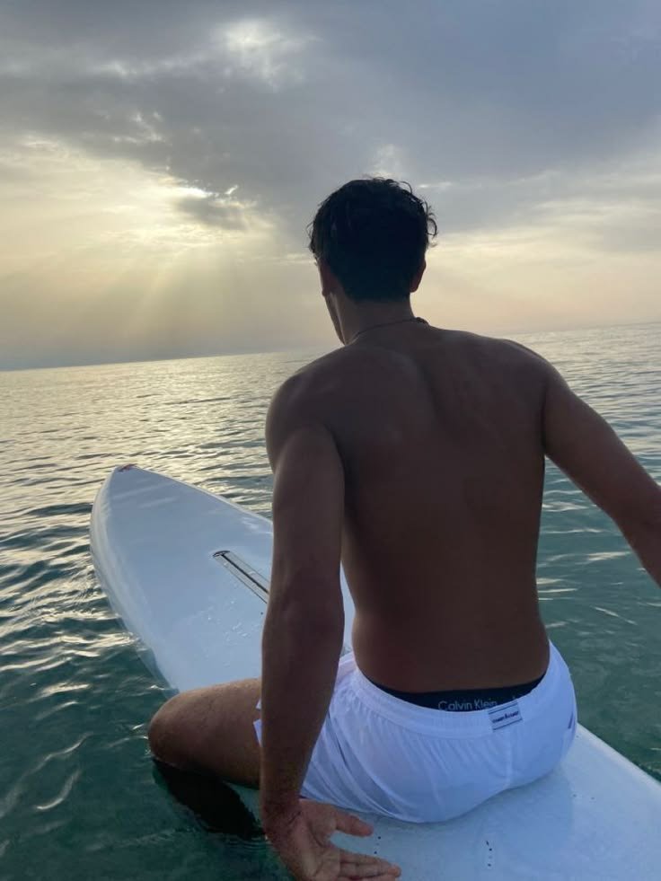 Chico de espaldas sentado sobre una tabla de paddle surf