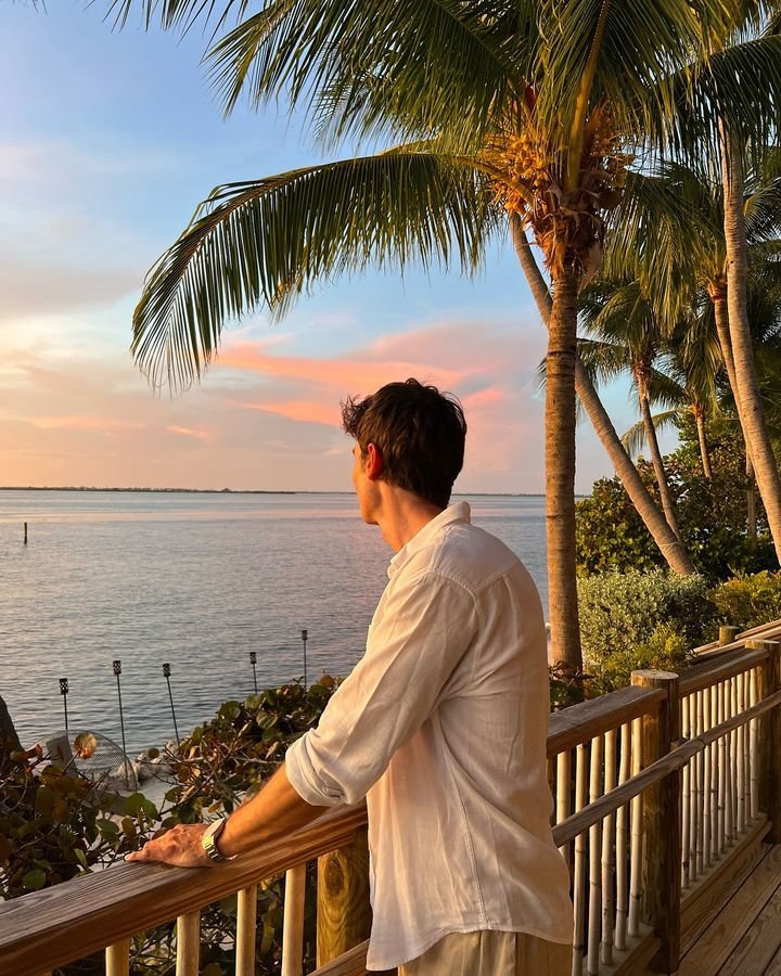 Chico apoyado en una barandilla entre palmeras al atardecer