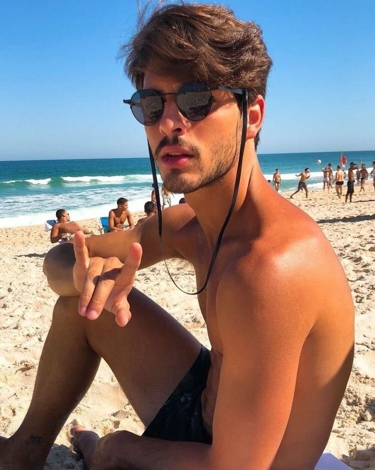 Chico sentado en la arena con gafas de sol