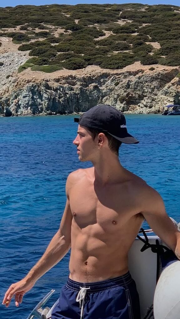 Chico de pie en un barco con gorra frente a un acantilado