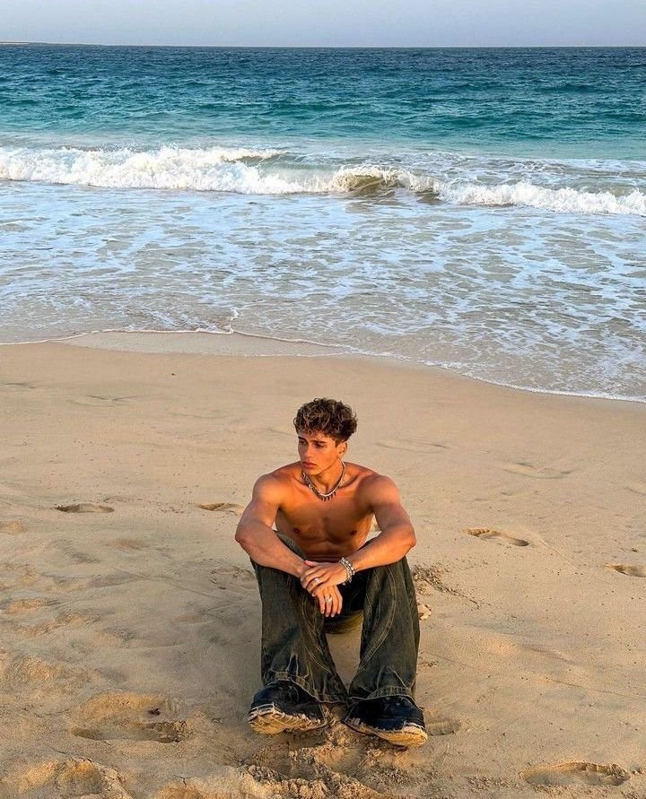 Chico sentado en la arena mirando al mar