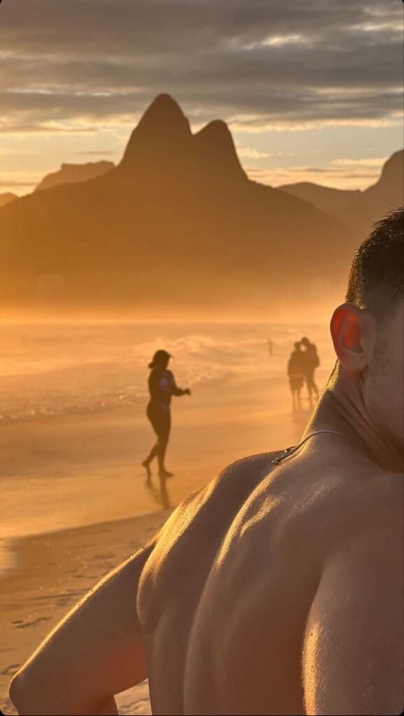 Chico de espaldas en la playa al atardecer con montañas
