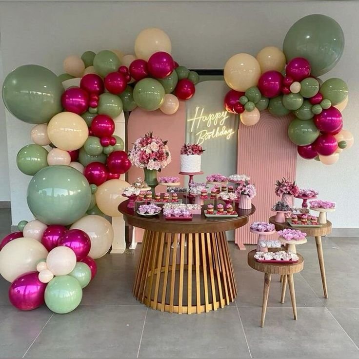 Arco de globos verde salvia y fucsia con mesa de postres