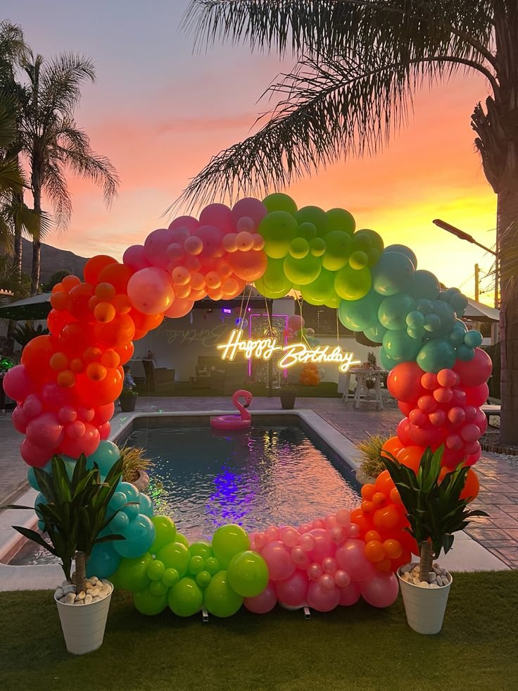 Arco circular de globos multicolor junto a una piscina al atardecer