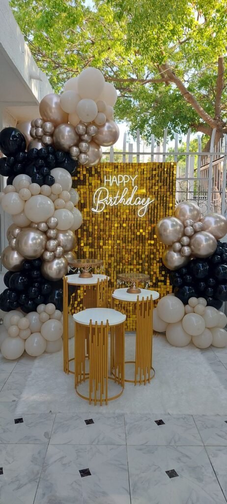 Decoración en globos beige y negros con mesas altas doradas