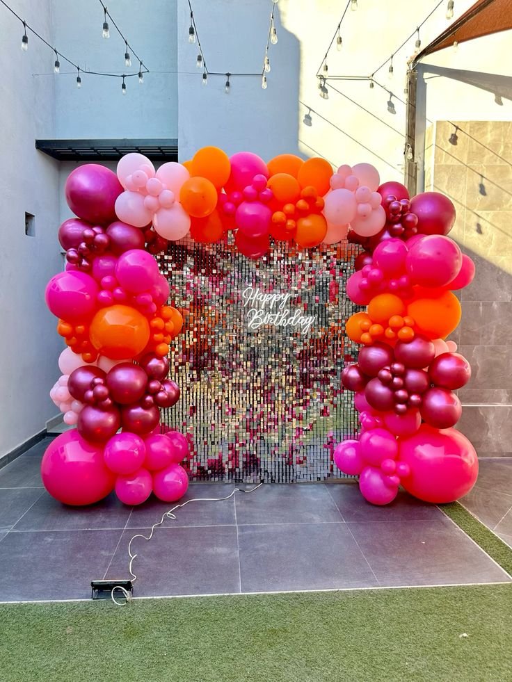 Arco de globos fucsia, rosa y naranja sobre césped