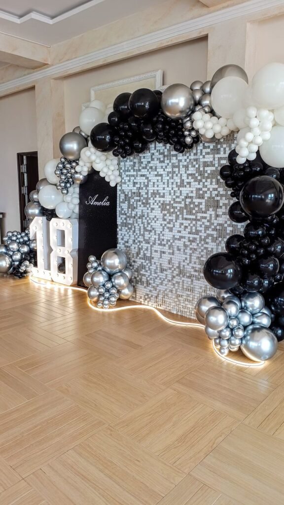 Arco de globos negros y plateados con fondo de lentejuelas