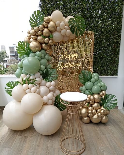 Panel de lentejuelas dorado con globos beige y hojas tropicales