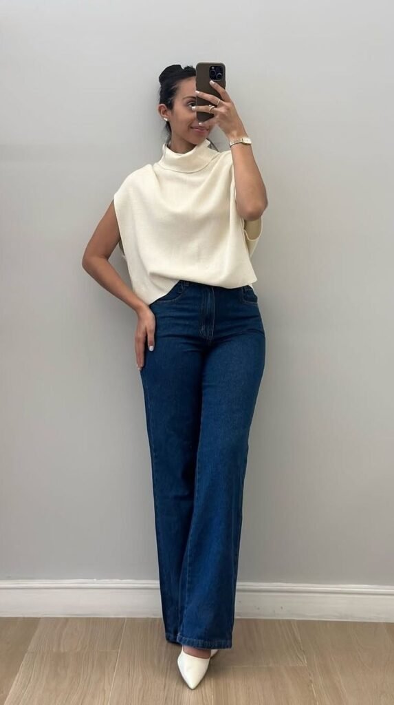 Top crema de cuello alto con jeans oscuros acampanados